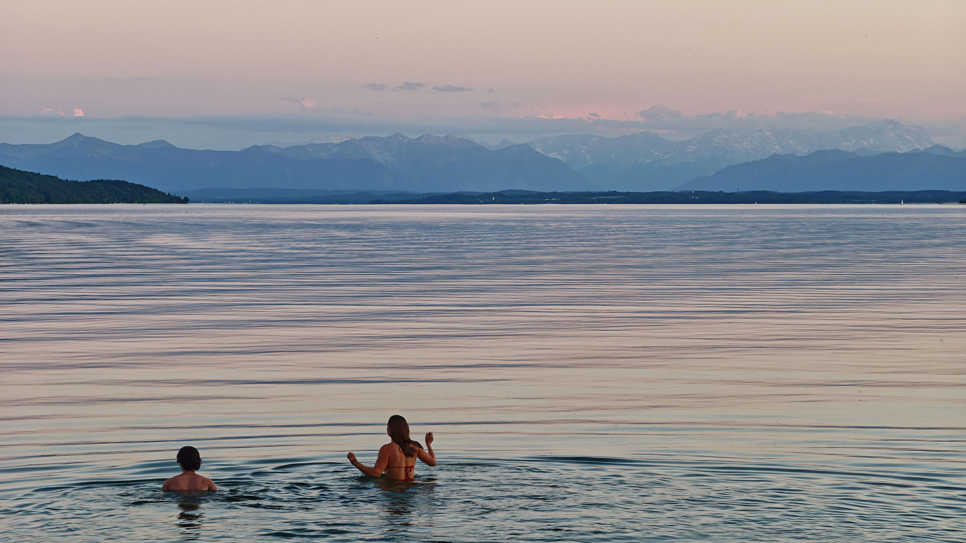 Two young people swim in Lake Starnberg at sunset in Starnberg, Upper Bavaria, Bavaria, Germany, on May 28, 2026. Warm evening weather brings visitors to the lake to cool off and spend quiet leisure time outdoors. 