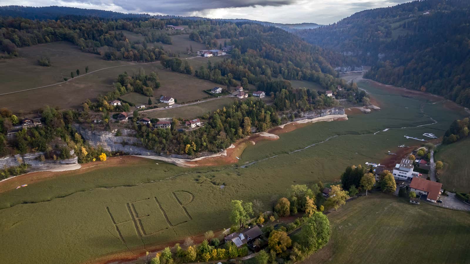 This aerial photograph shows a giant "Help" written by local residents on the grass-covered bed of the previously parched Lake Brenets, part of the Doubs River forming a natural border between eastern France and western Switzerland, in Les Brenets, Switzerland, on Oct. 1, 2026. The river has dried up in July 2026 due to a combination of factors, including geological fissures that drain water underground, below-average rainfall and repeated heatwaves and could surpass soon the drought record set in 1906.