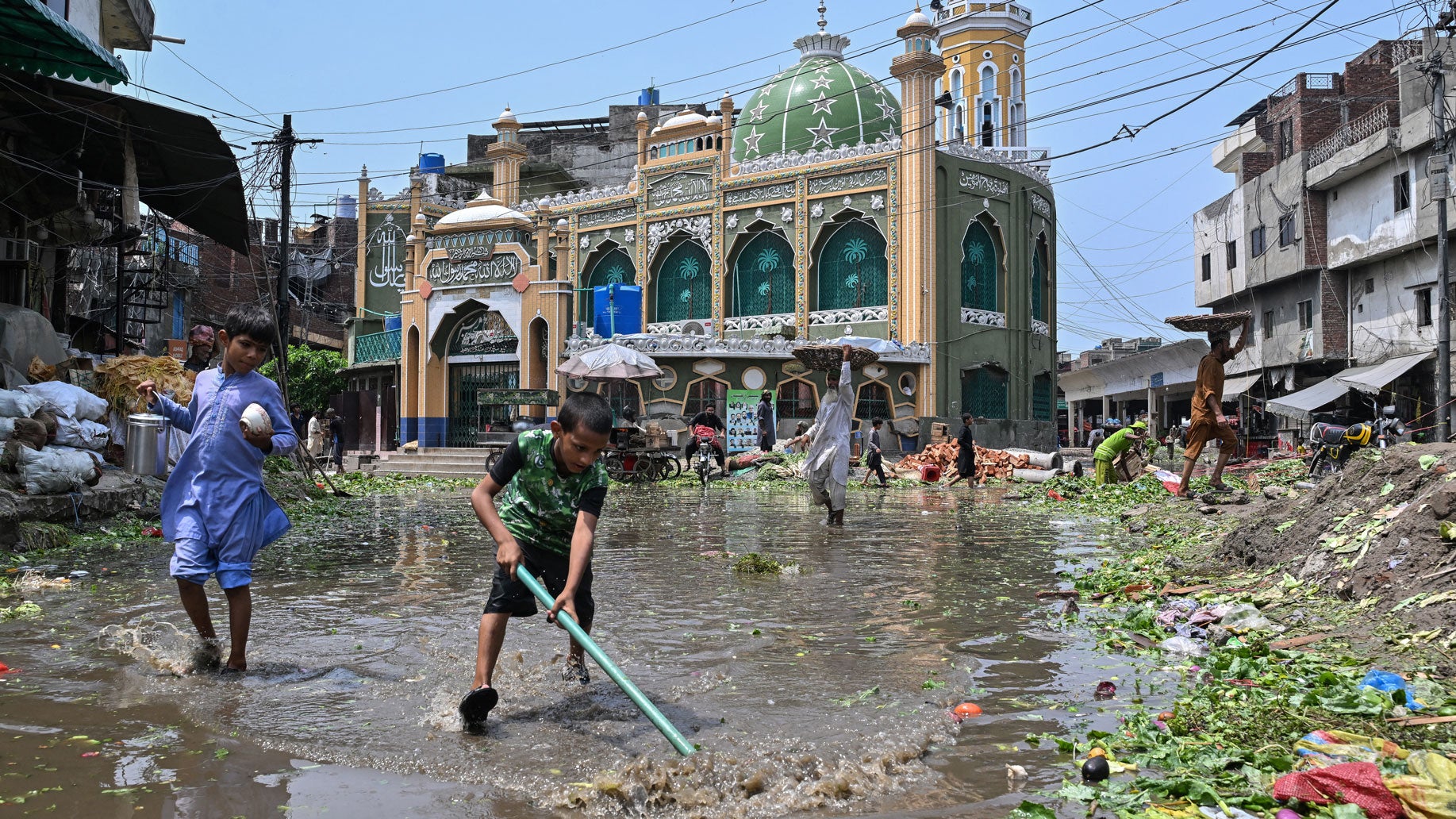 A boy removes vegetable waste floating on a waterlogged road at a market following heavy rainfall in Lahore, Pakistan on Aug. 6, 2026. 