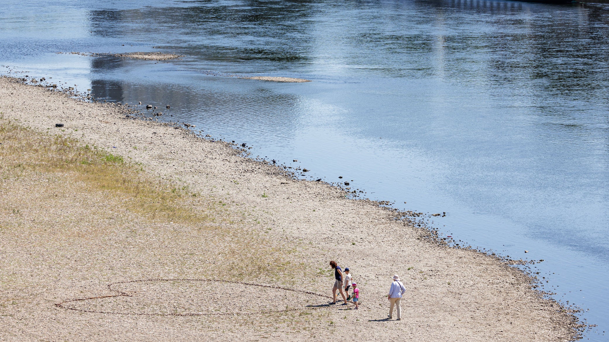 People walk on the long riverbed of the Elbe River, where a heart is drawn on the ground in Dresden, eastern Germany, on Sunday, Aug. 9, 2026. Dry weather conditions are keeping the water level of the river very low. 