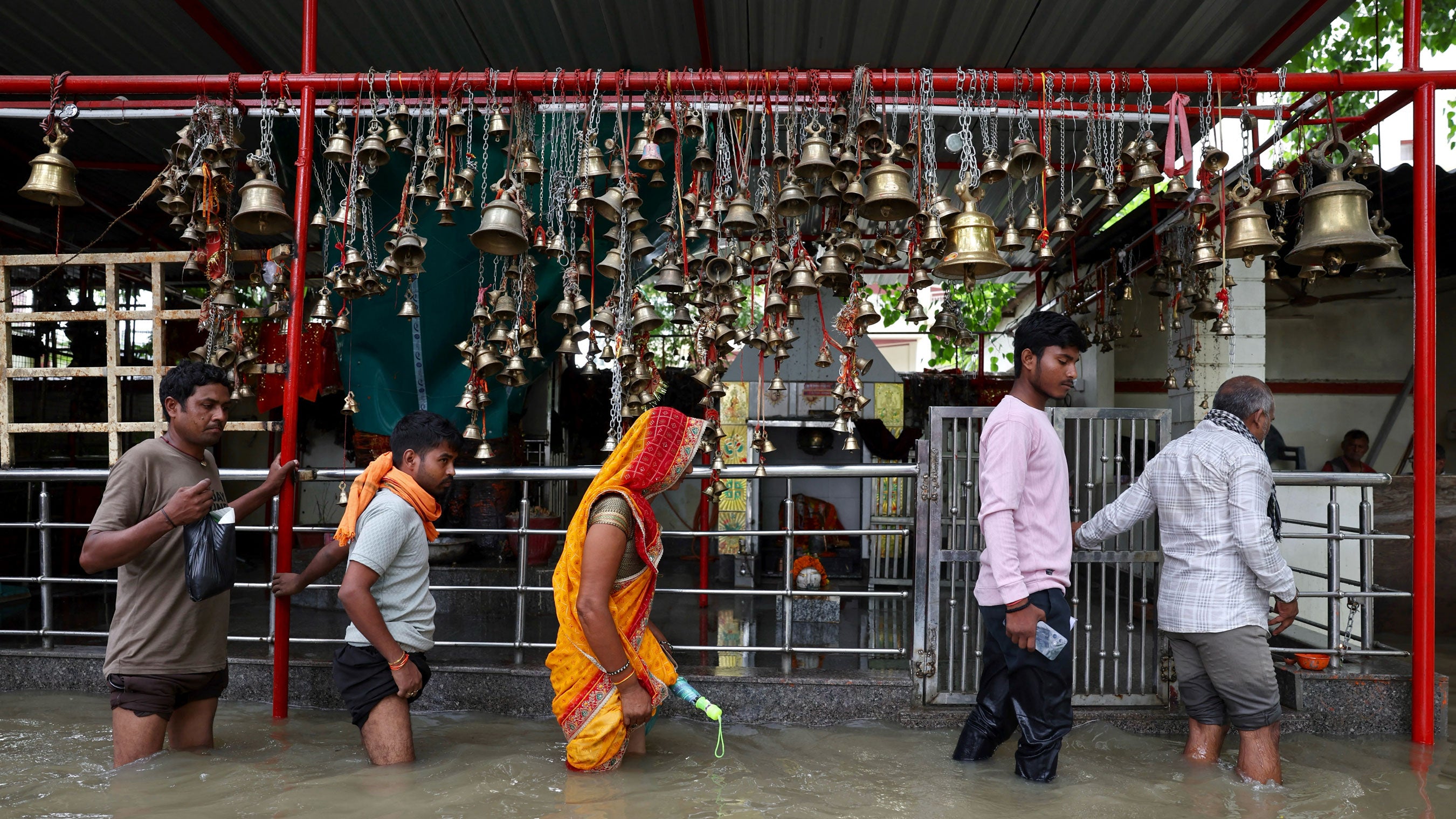 People wade through a waterlogged street in front of a temple after heavy rain in Varanasi, India on Tuesday, Aug. 25, 2026.