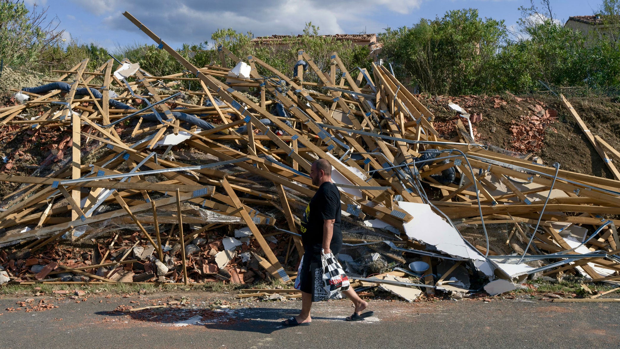 A man walks past debris of a damaged rooftop following a tornado in Pomas, southwestern France on Tuesday, Aug. 25, 2026. A tornado of rare intensity devastated a village in southern France, causing widespread destruction and leaving residents in shock, with the mayor describing the aftermath as resembling "wartime." The tornado brought down walls, tore off roofs and uprooted trees.