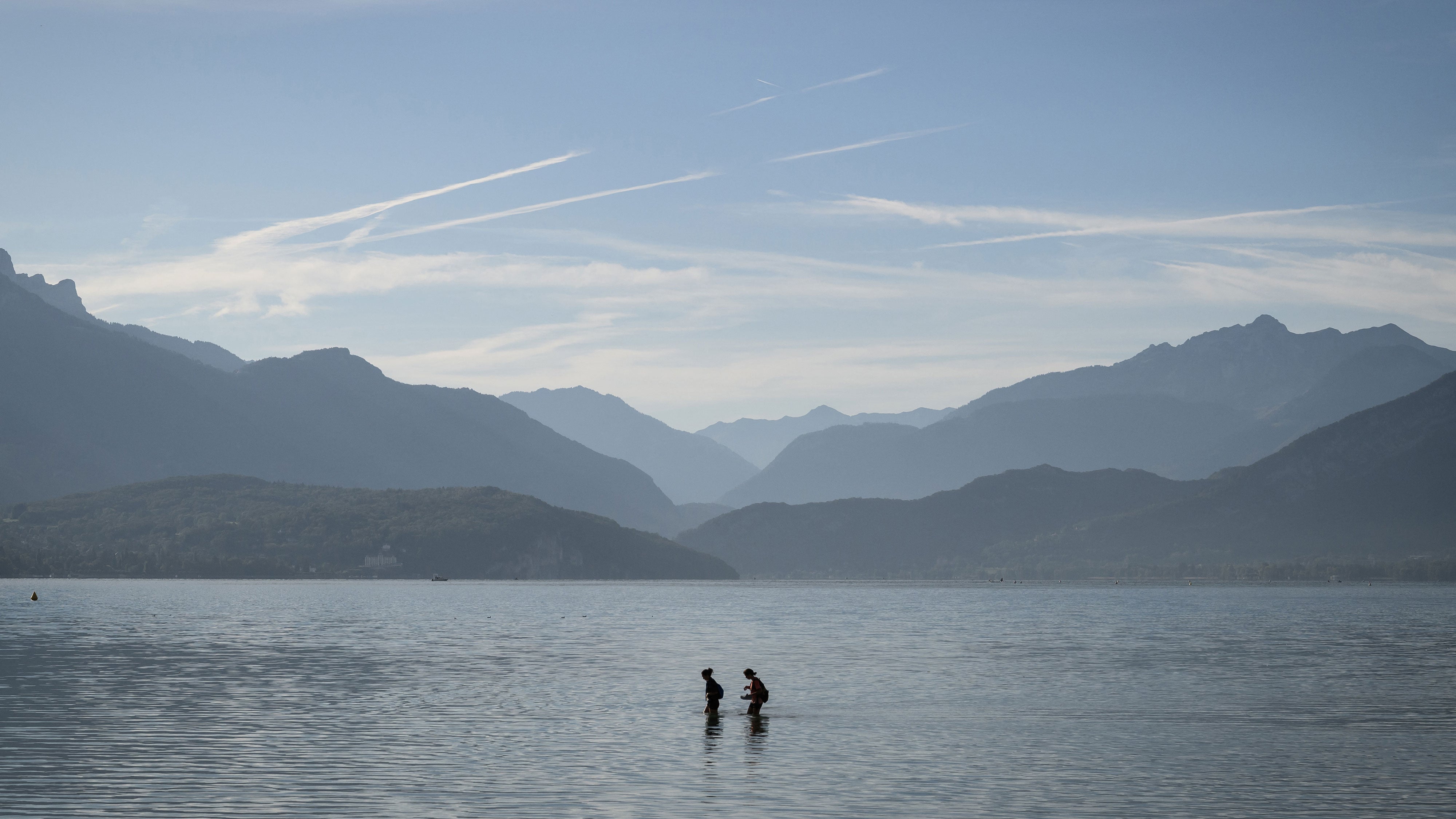 Two people wade through the shallow water of Lake Annecy, far from the shore, as the water level has dropped significantly due to the drought, in Annecy, France, on Sept. 24, 2026.